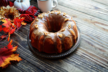 Delicious, Pumpkin Spice Bundt Cake Frosted With Brown Sugar Frosting And Walnuts With Autumn Leaves And Coffee Over A Rustic Wooden Table Background. Image Shot From Above..