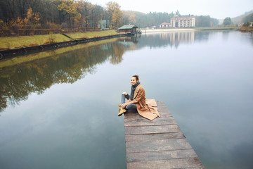 Happy woman sitting on the wooden pier in the park at autumn.