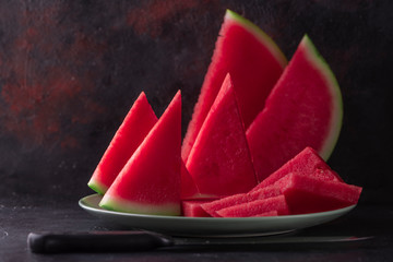 Wall Mural - Fresh sweet spanish watermelon sliced on green plate on dark background. Low key close up shot with selective focus