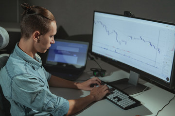 Young male programmer working late at night, copy space. Male stock trader using two computers, working in a dark office room