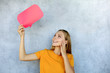 © ty - Happy beautiful young blonde woman standing isolated over gray background, holding empty speech bubble