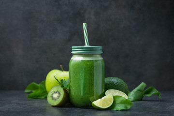 Wall Mural - Green detox smoothie in glass jar from spinach, kiwi, lime, avocado on a dark stone table