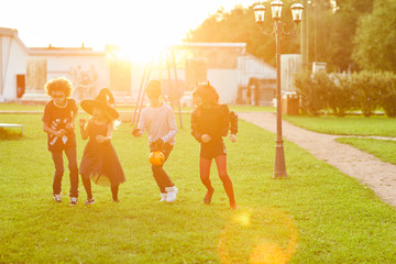 Wall Mural - Multi-ethnic group of kids wearing Halloween costume shaving fun running outdoors lit by sunlight, copy space