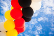 Balloons - Colors of the German National Flag (black, red, yellow)  - outdoors against blue Sky with white Clouds - Symbol for Festivity or Celebration