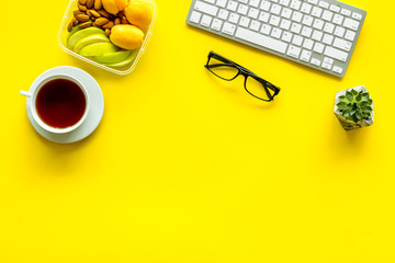 Wall Mural - Food container with healthy food on office desk with keyboard and tea on yellow background top view mockup