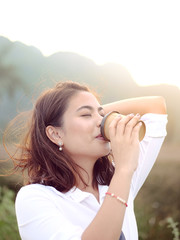  Emotional Asian woman drinkng take away coffee cup with sun light outdoor, lifestyle concept.