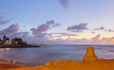 Wall Mural - Morning just before sunrise on the Mediterranean south of the port city of Torrevieja. The still lit city can be seen in the background. In the foreground a small bay. Long Exposure.