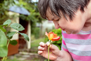 Wall Mural - Frau mit geistiger Behinderung riecht an einer Rose im Garten, Bewusstsein und Selbstbestimmung