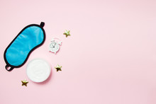 Blue Sleeping Eye Mask, Alarm Clock And Jar Of Cream On Pink Background. Night Skin Care Concept