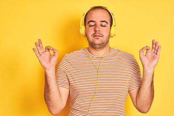 Sticker - Young man listening to music using headphones standing over isolated yellow background relax and smiling with eyes closed doing meditation gesture with fingers. Yoga concept.