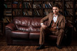 © Ilnur - young successful man in a brown kosmtyum drinks whiskey. bearded businessman sitting in a library on a luxurious leather sofa and drinking cognac