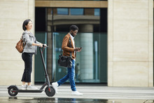 Full Length Portrait Of People Commuting In City, Focus On Asian Woman Riding Electric Scooter In Foreground, Copy Space