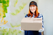 Delivery Woman In Navy Bkue Uniform Isolated On Colorful Background. Female In Cap, T-shirt, Jeans Working As Courier Or Dealer Holding Cardboard Box. Receiving Package. Copy Space Advertisement.