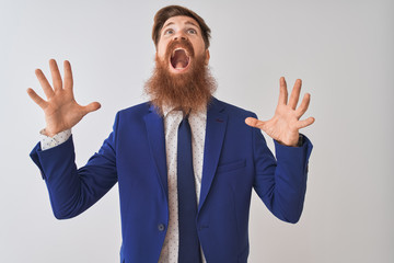 Canvas Print - Young redhead irish businessman wearing suit standing over isolated white background crazy and mad shouting and yelling with aggressive expression and arms raised. Frustration concept.