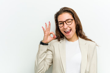 Wall Mural - Young european business woman winks an eye and holds an okay gesture with hand.