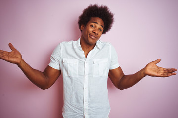 Poster - Young american man with afro hair wearing white shirt standing over isolated pink background clueless and confused expression with arms and hands raised. Doubt concept.