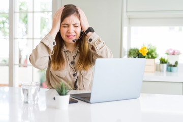 Canvas Print - Beautiful young operator woman working with laptop and wearing headseat suffering from headache desperate and stressed because pain and migraine. Hands on head.