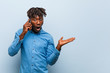 © Asier - Young rasta black man holding a phone impressed holding copy space on palm.