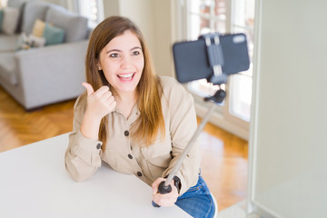 Canvas Print - Beautiful young woman taking a picture using selfie stick happy with big smile doing ok sign, thumb up with fingers, excellent sign