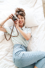 Poster - Happy cheery positive woman indoors at home lies on bed in the morning holding camera photographing.