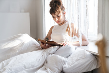 Canvas Print - Beautiful lady lies in bed indoors at home reading book.