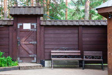 Close-up on a brown wooden door with forged iron hinged patterns and two old benches.