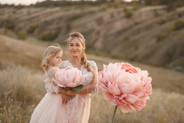 Mom with daughter in pink fairy-tale dresses walk in nature. The childhood of the little princess. Large pink decorative flowers