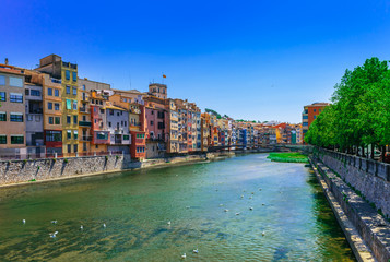 Wall Mural - Colorful red, orange and yellow houses and bridge through river Onyar in Girona, Catalonia, Spain. Scenic ancient town. Famous tourist resort destination perfect place for holiday and vacation