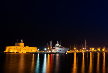 Wall Mural - Night photo of ancient fortress and pier in Rhodes city on Rhodes island, Dodecanese, Greece. Stone walls and bright night lights. Famous tourist destination in South Europe