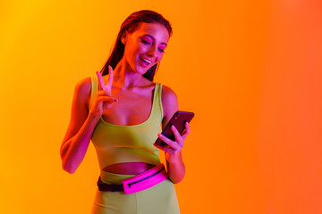 Sticker - Image of fashionable brunette woman wearing formfitting sportswear smiling while using smartphone for video call