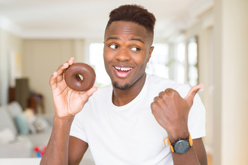 Sticker - African american man eating chocolate donut pointing and showing with thumb up to the side with happy face smiling