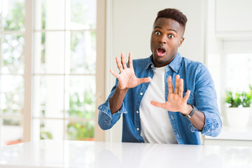 Wall Mural - Handsome african american man at home afraid and terrified with fear expression stop gesture with hands, shouting in shock. Panic concept.