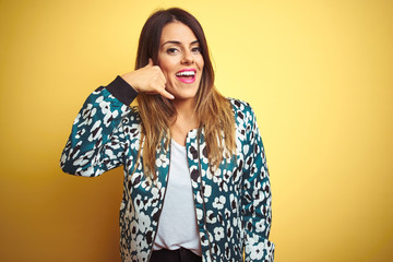 Wall Mural - Young beautiful woman wearing casual jacket over yellow isolated background smiling doing phone gesture with hand and fingers like talking on the telephone. Communicating concepts.