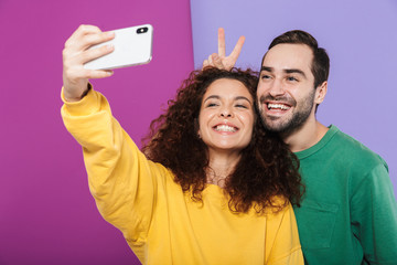 Sticker - Portrait of funny caucasian couple in colorful clothing having fun while taking selfie photo on cellphone