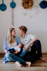 Wall Mural - A portrait of beautiful young parents with a newborn baby at home.