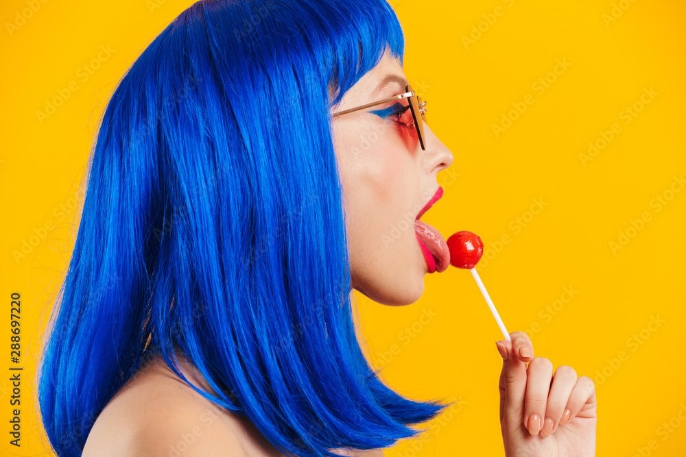 Portrait in profile of glamorous nice young woman wearing blue wig and sunglasses licking lollipop - obrazy, fototapety, plakaty 