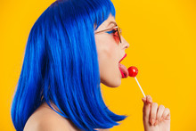 Portrait In Profile Of Glamorous Nice Young Woman Wearing Blue Wig And Sunglasses Licking Lollipop