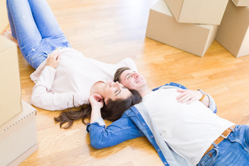 Poster - Young beautiful couple relaxing lying on the floor around cardboard boxes at home, smiling happy moving to a new house