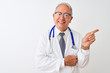 © Krakenimages.com - Senior grey-haired doctor man wearing stethoscope standing over isolated white background with a big smile on face, pointing with hand and finger to the side looking at the camera.