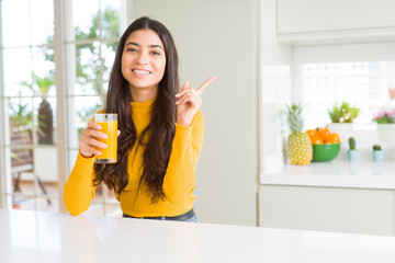 Young woman drinking a glass of fresh orange juice very happy pointing with hand and finger to the side