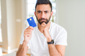 Sticker - Handsome hispanic man holding credit card serious face thinking about question, very confused idea