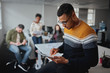 © StratfordProductions - Professional young businessman using digital tablet with colleagues working at office in the background