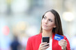 Doubtful woman holding credit card and cell phone