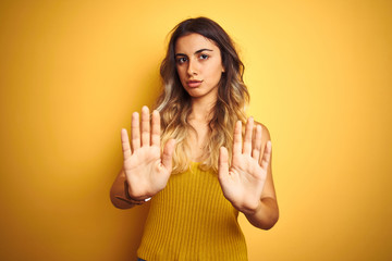 Canvas Print - Young beautiful woman wearing t-shirt over yellow isolated background Moving away hands palms showing refusal and denial with afraid and disgusting expression. Stop and forbidden.