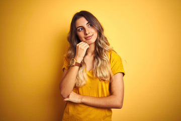 Canvas Print - Young beautiful woman wearing t-shirt over yellow isolated background with hand on chin thinking about question, pensive expression. Smiling with thoughtful face. Doubt concept.