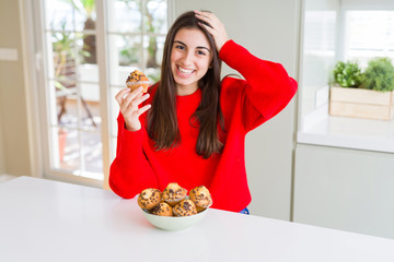 Sticker - Beautiful young woman eating chocolate chips muffins stressed with hand on head, shocked with shame and surprise face, angry and frustrated. Fear and upset for mistake.