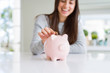 © Krakenimages.com - Young woman smiling putting a coin inside piggy bank as savings for investment