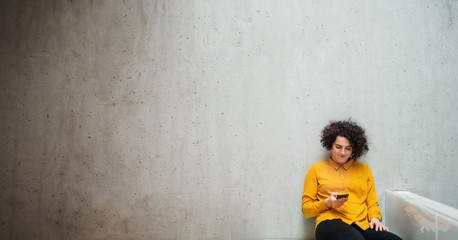 Wall Mural - Young student or businesswoman with smartphone sitting on desk in room in a library or office.