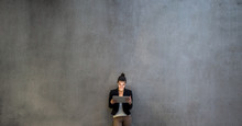 Young Business Woman With Tablet Standing Against Concrete Wall In Office.