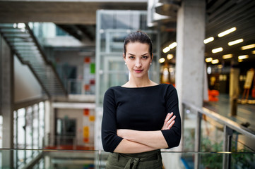 A portrait of young businesswoman standing in corridor outside office, arms crossed.